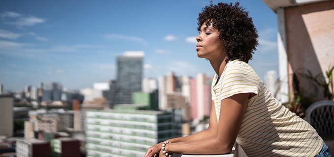 Women on balcony taking deep breath, eyes closed facing sunrise